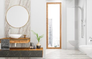 Modern bathroom interior with minimalist design elements, featuring a sleek vanity with a vessel sink installed by a professional plumber, circular mirror, and a view of the cityscape through the adjacent glass door.